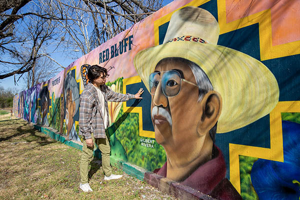 Artist Ruben Esquivel posing with his mural, Protectors of the Red Bluff, depicting his uncles