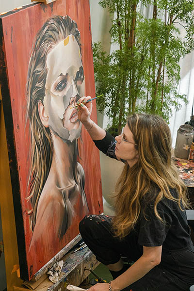 Montreal artist Sandra Chevrier working on a portrait of a woman in a mask